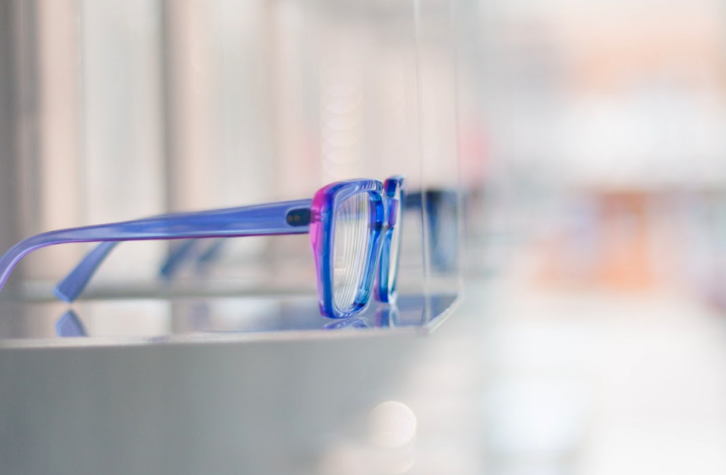 A side view of a pair of Kirk and Kirk glasses, sitting on a clear display shelf at CHROMA modern Eyewear Eyecare