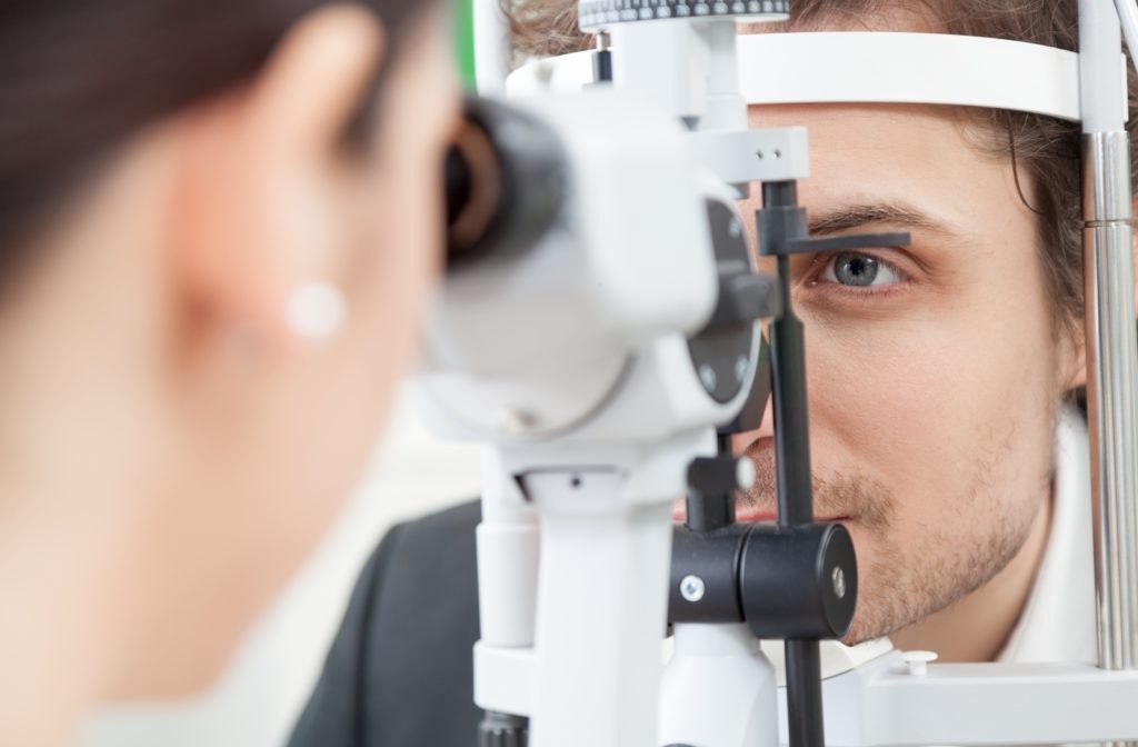 A close up of a man getting an eye exam while his optometrist is using a slit lamp