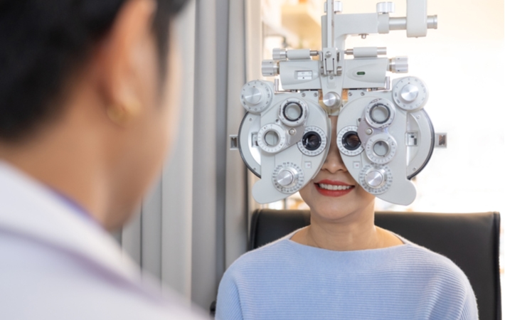 A woman smiling while she is undergoing a refraction test as part of her eye exam to help determine what level of the prescription she needs for her eyeglasses