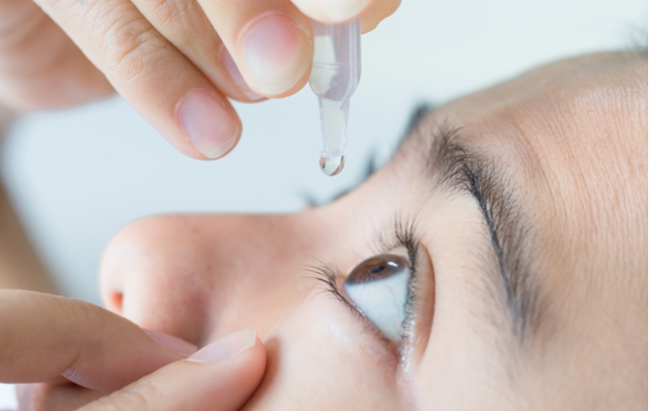 A close up side view of a woman using eye drops to help treat her dry eye