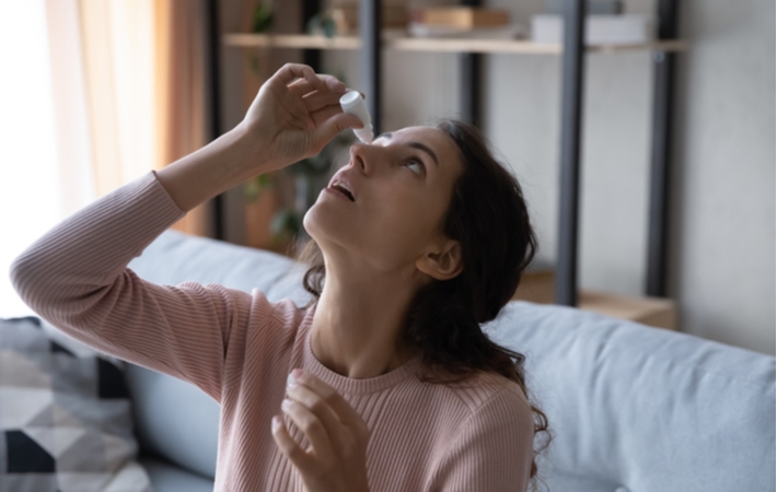 A woman tilting her head back as she is using eye drops to help improve her presbyopia