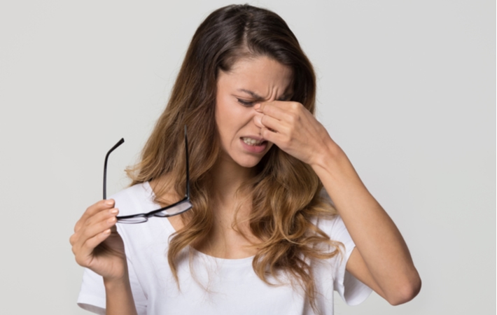 A woman taking her glasses off as she rubs her eyes in frustration due to the discomfort of her dry eye