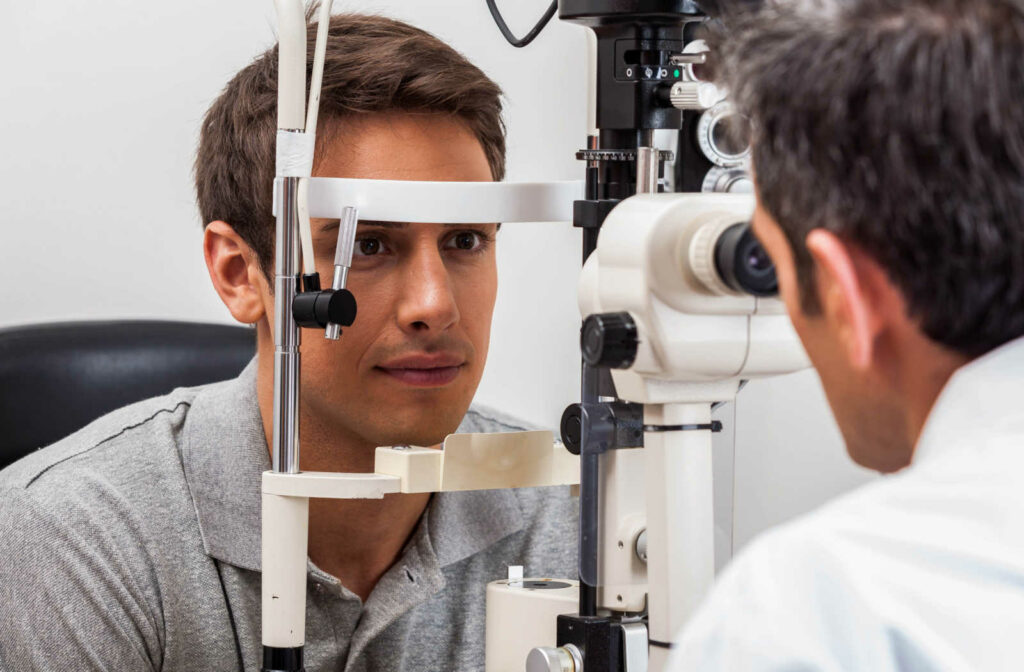 A man is sitting in front of a Keratomer and looking through it while the male optician is looking through it on the other side.
