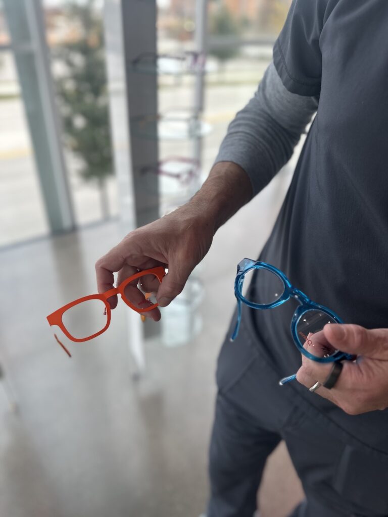 Dr. Barber holding an orange and blue pair of Lindberg frames at the CHROMA practice in Fort Worth, Texas.