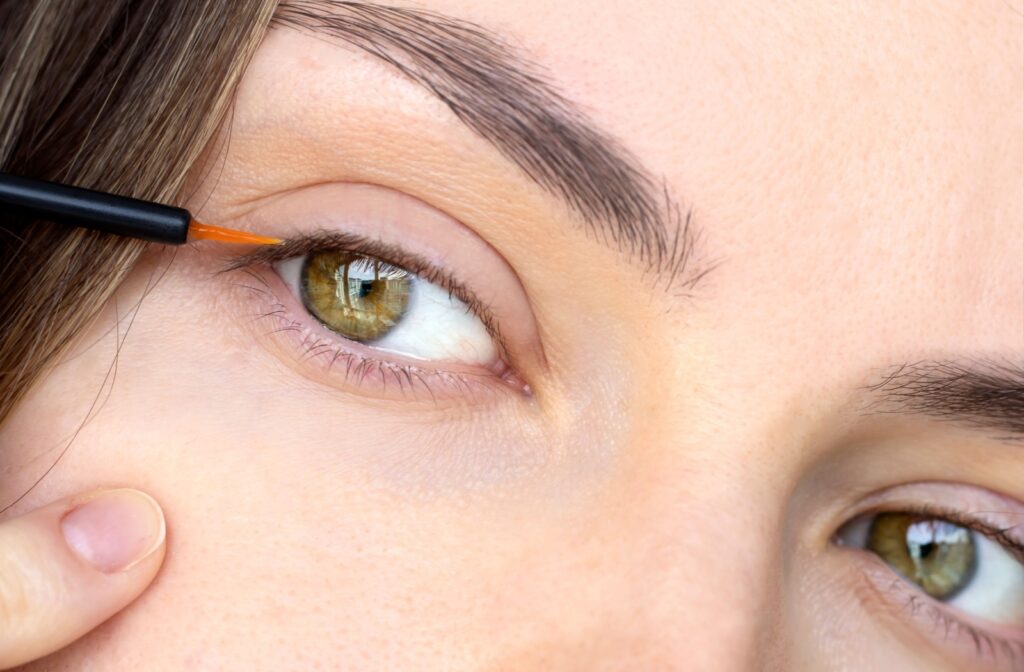 An extreme close up of a dark-haired person's hazel eyes getting an eyelash boosting serum like Latisse added to their lash line.