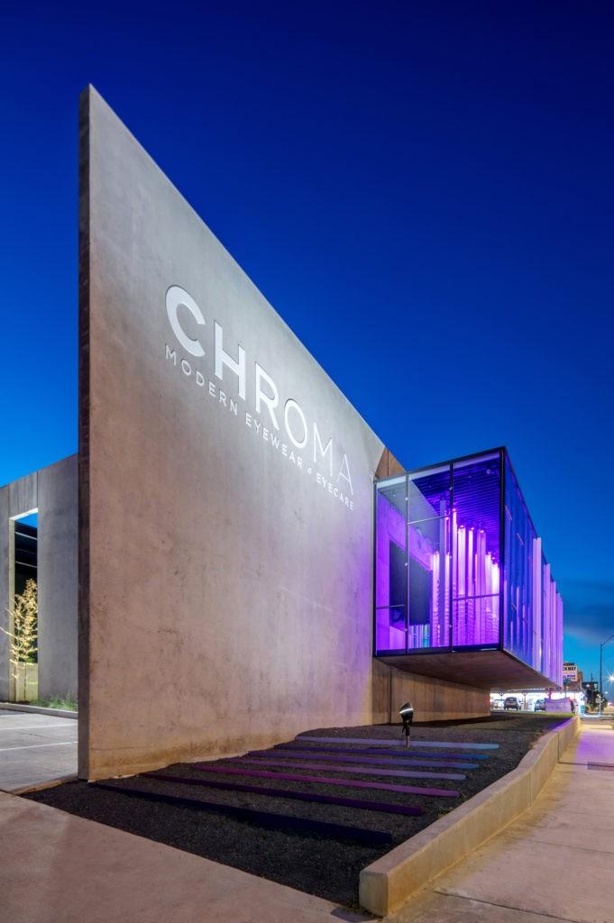 Exterior of CHROMA modern Eyewear Eyecare with illuminated signage and purple lighting at dusk.