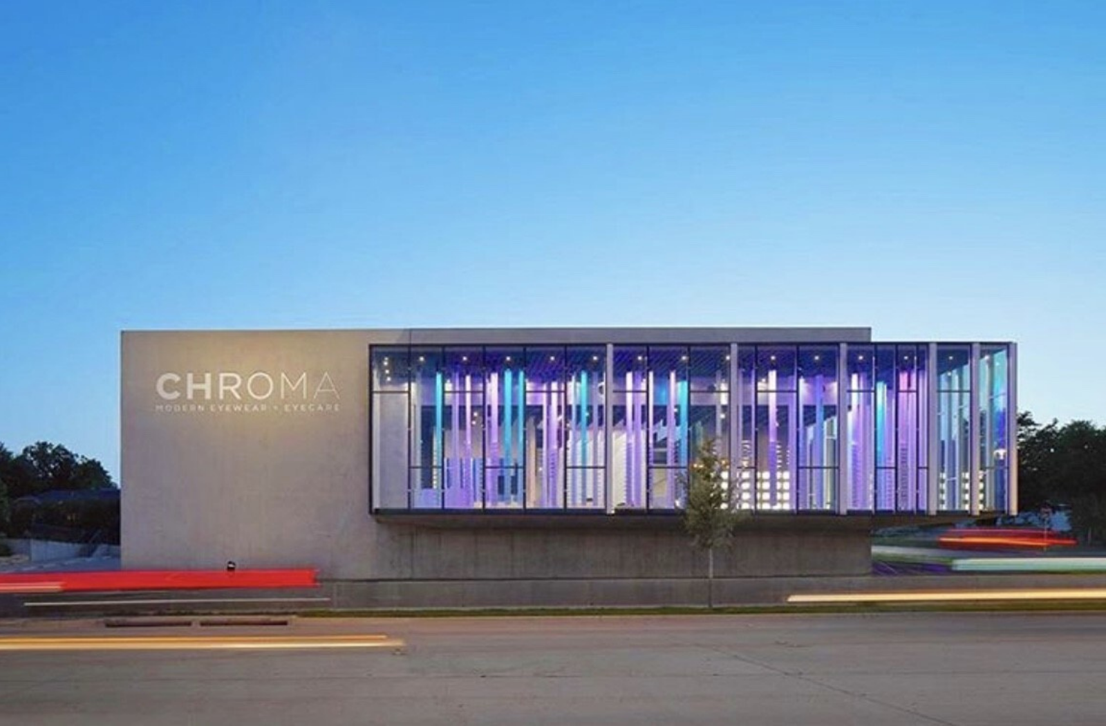 Exterior of CHROMA Modern Eyewear & Eyecare with colourful illuminated windows at dusk.